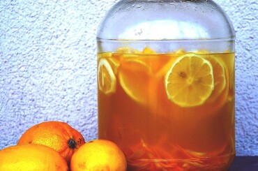 Переложить цедру лимона и нарезанный кружочками лимон в трехлитровую стеклянную банку, залить сахарным сиропом и добавить водку или спирт. Взболтать. Закрутить плотно крышкой и поставить настаиваться на 5 дней.