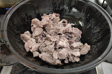 Перекладываем подваренное мясо кабана в разогретый казан. Обжариваем мясо на сильном огне 2-3 минуты.